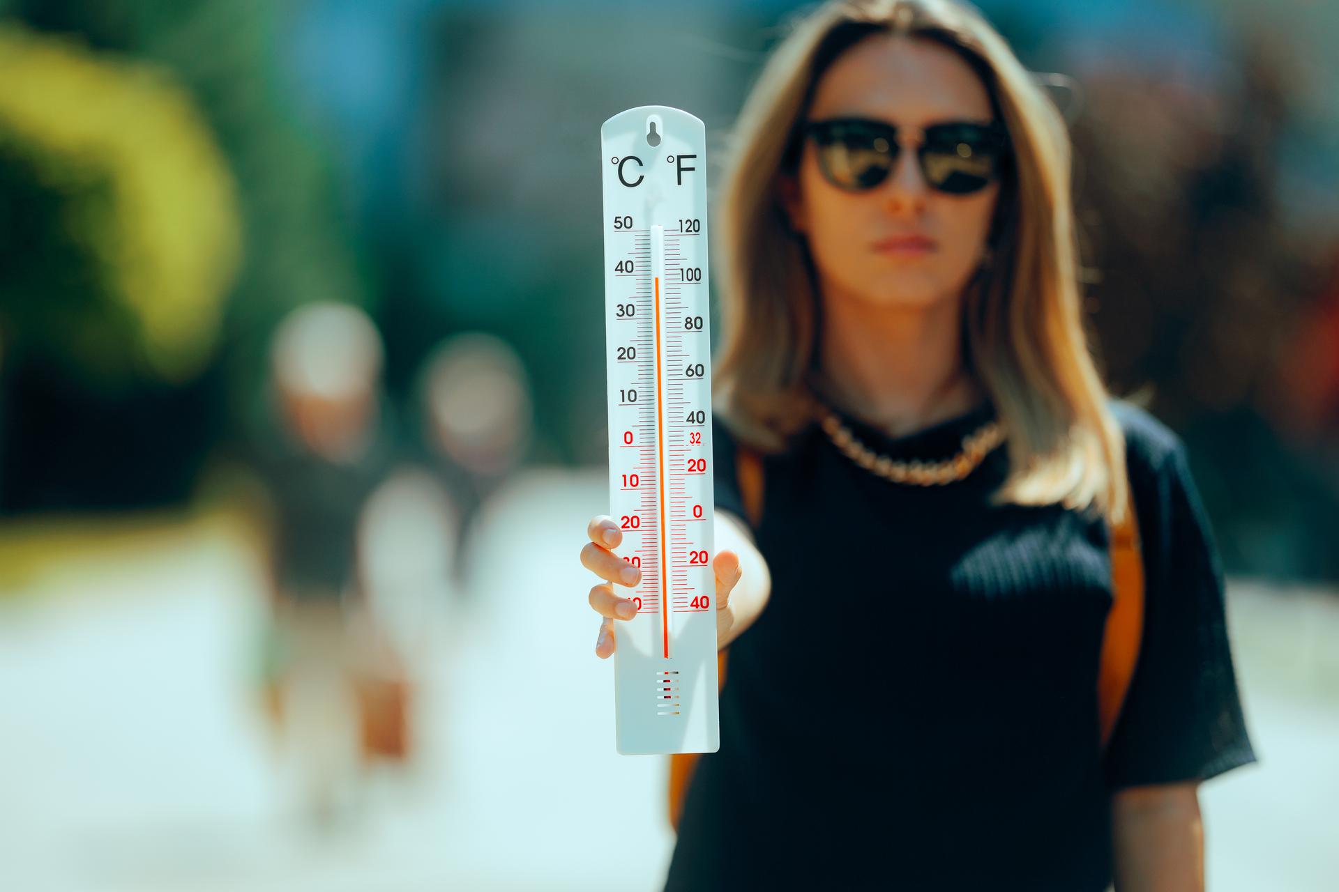 Woman holding an Outdoors thermometer Showing High Temperatures